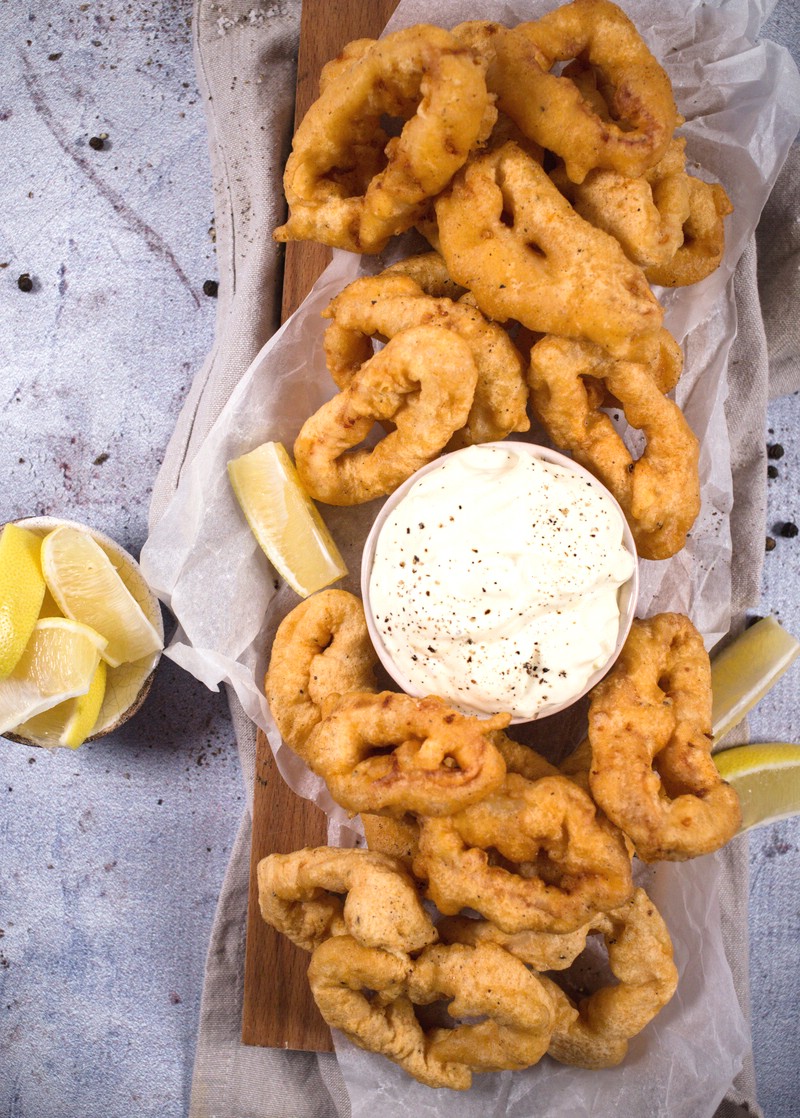 Fried squid on a platter with dipping sauce and lemon slices
