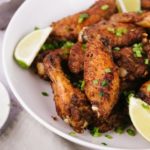 Salt and pepper chicken wings on white plate with lime wedge