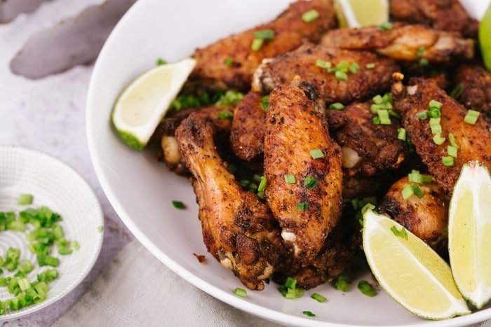 Salt and pepper chicken wings on white plate with lime wedge