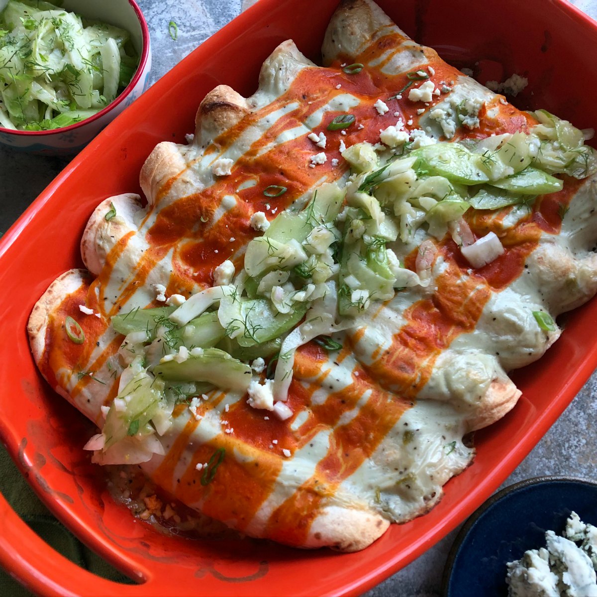 orange casserole dish filled with enchiladas on gray table