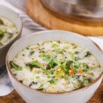 Onion soup with green vegetables in large white bowl