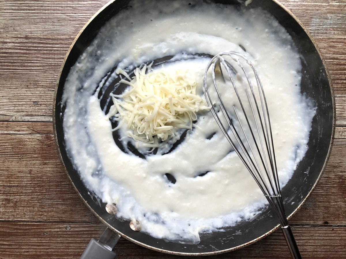 Cheese sauce being whisked in cast iron skillet