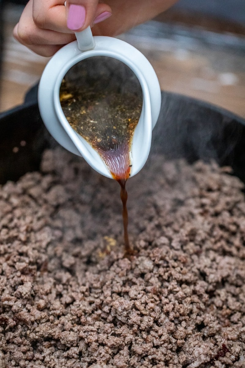 Pouring sauce into ground beef in skillet