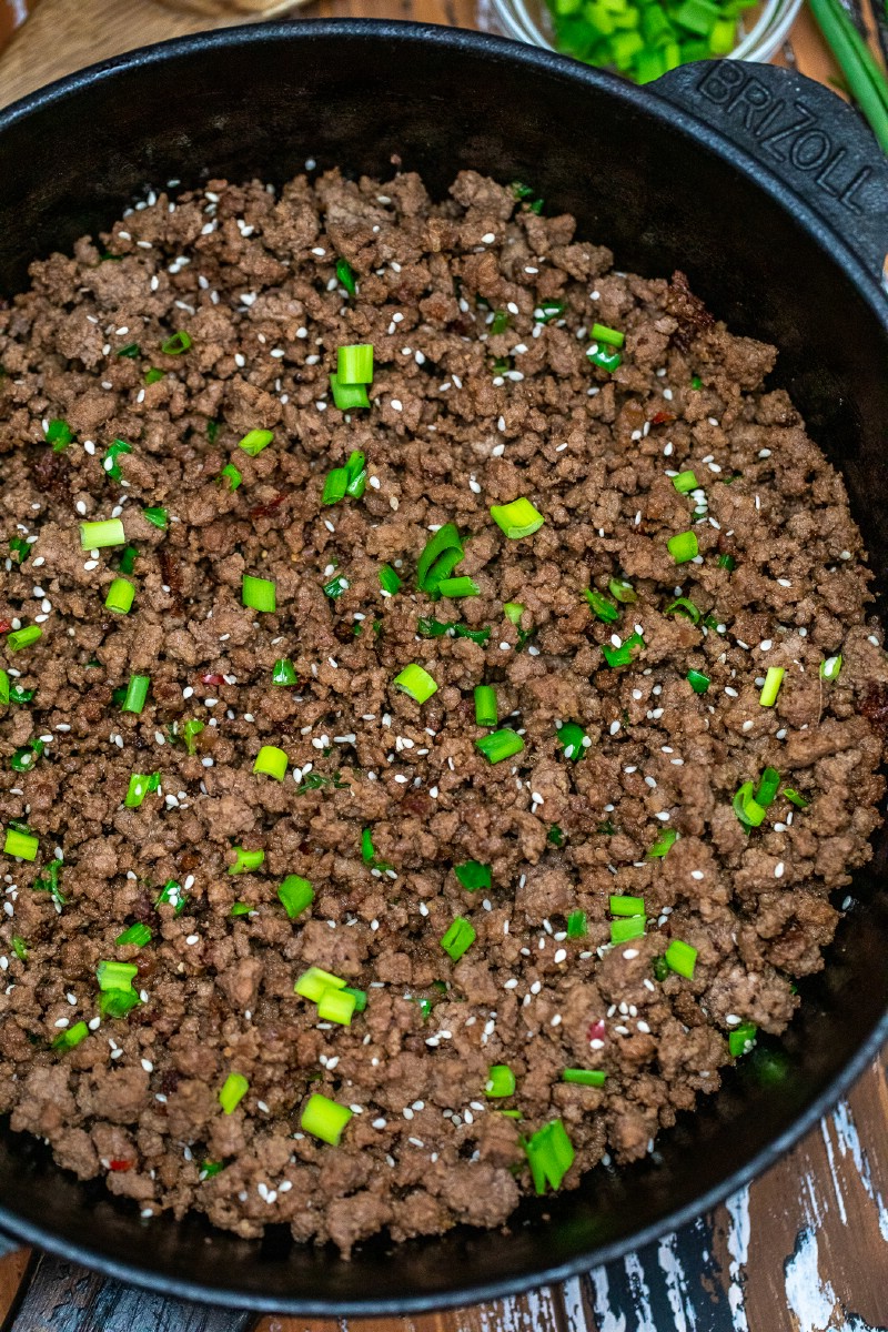 Ground beef and green onions being cooked in cast iron skillet