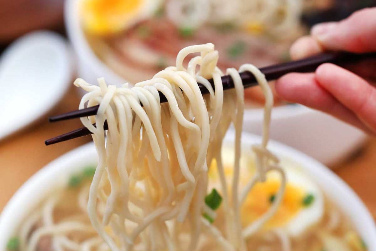 Chopsticks holding ramen noodles above bowl