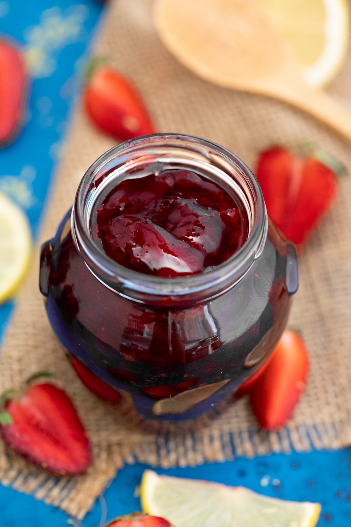 Pear shaped jam jar with strawberry jam on burlap and blue napkins 