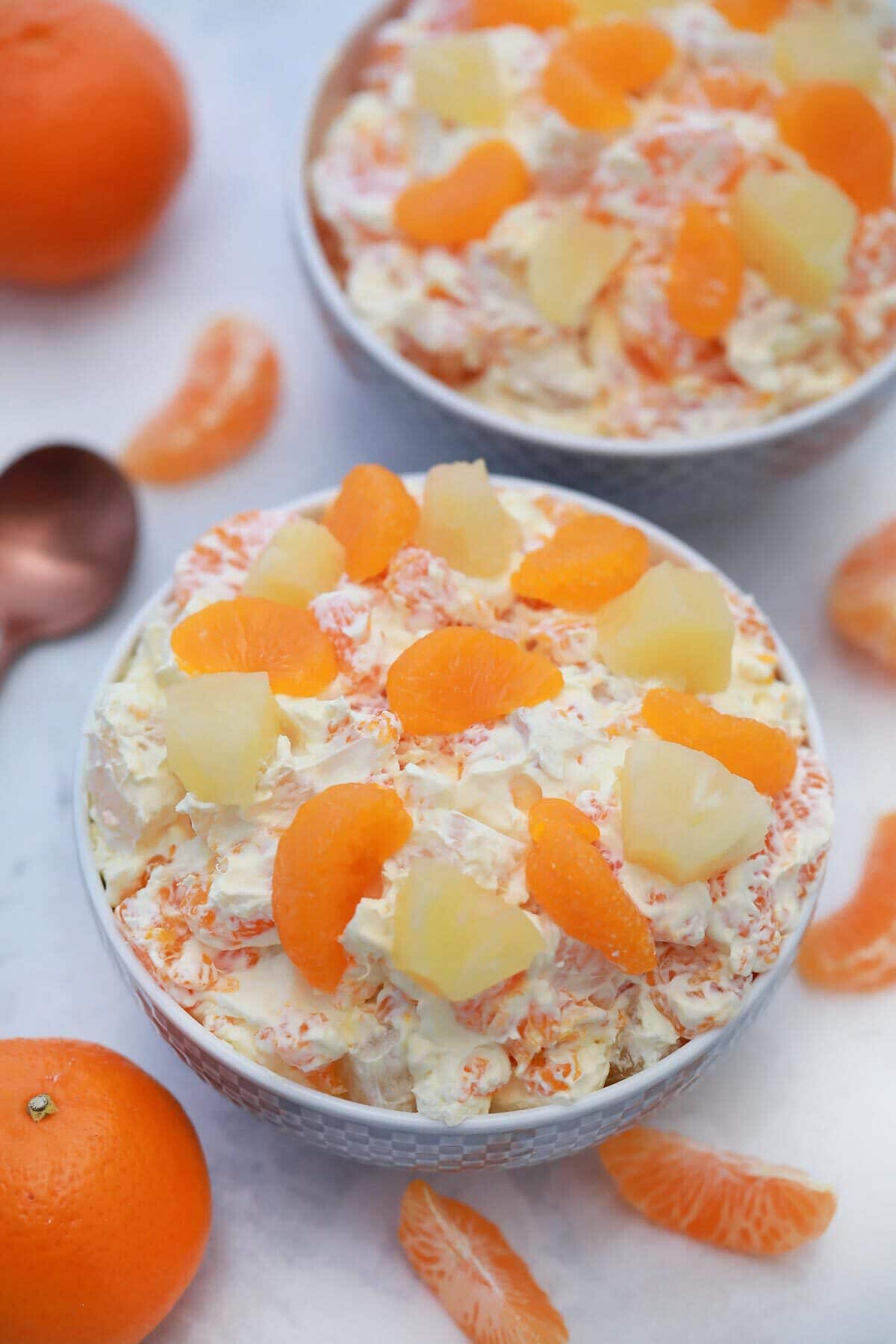 Two white bowls filled with orange cream salad topped with sliced orange and pineapples