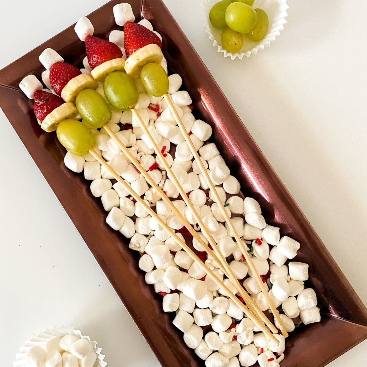 Grinch kabob on platter with marshmallows, grapes, banana, and strawberries.