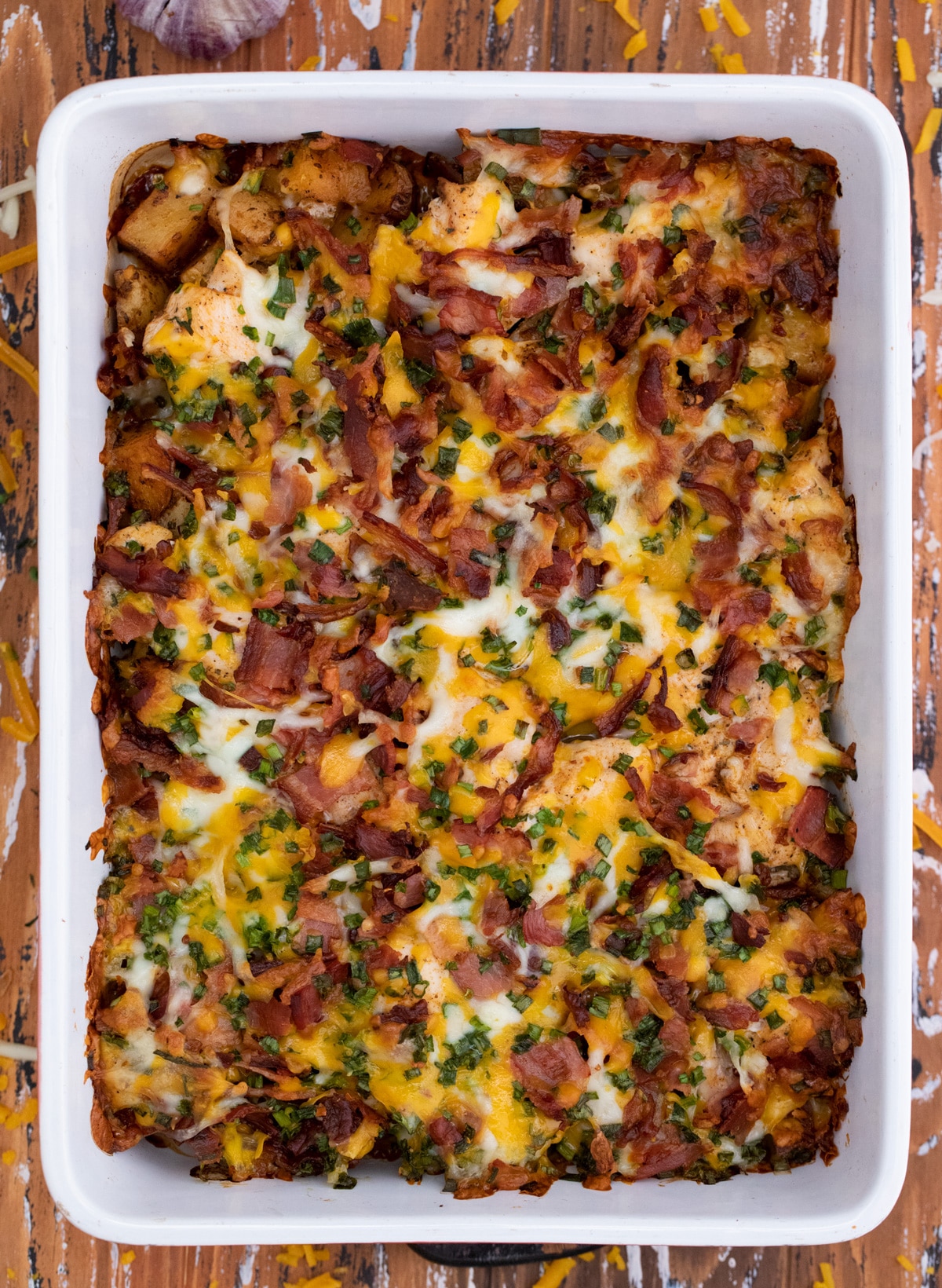 White casserole dish filled with loaded potato casserole topped with cheese and bacon