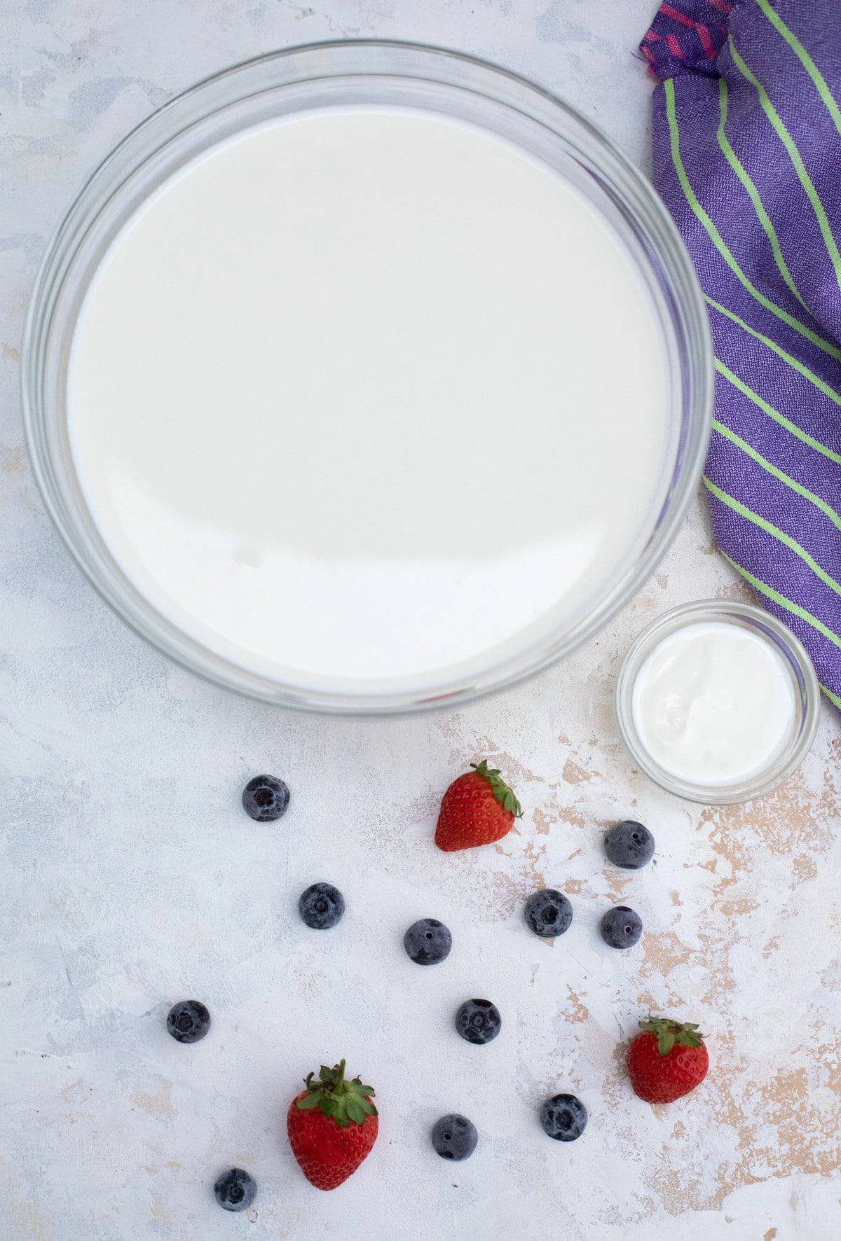 Glass jar of yogurt with berries beside it on table.