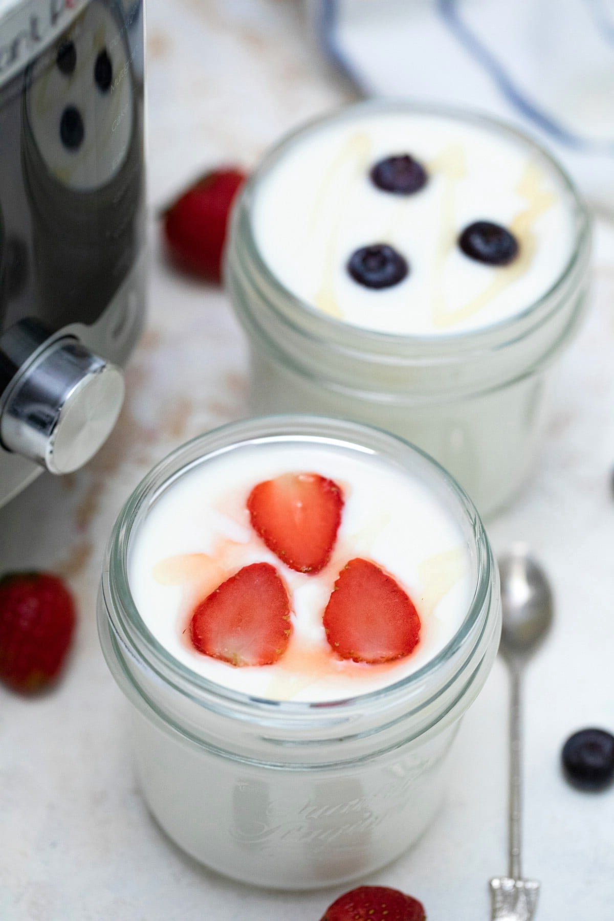 Glass jars of yogurt topped with strawberry and blueberry on white table.