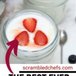 Glass jars of yogurt topped with strawberry and blueberry on white table.