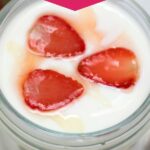 Glass jars of yogurt topped with sliced strawberries and honey