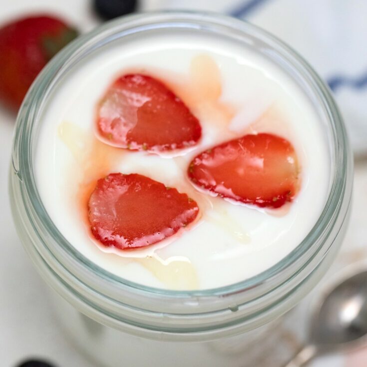 Yogurt in glass mason jar topped with strawberry and honey