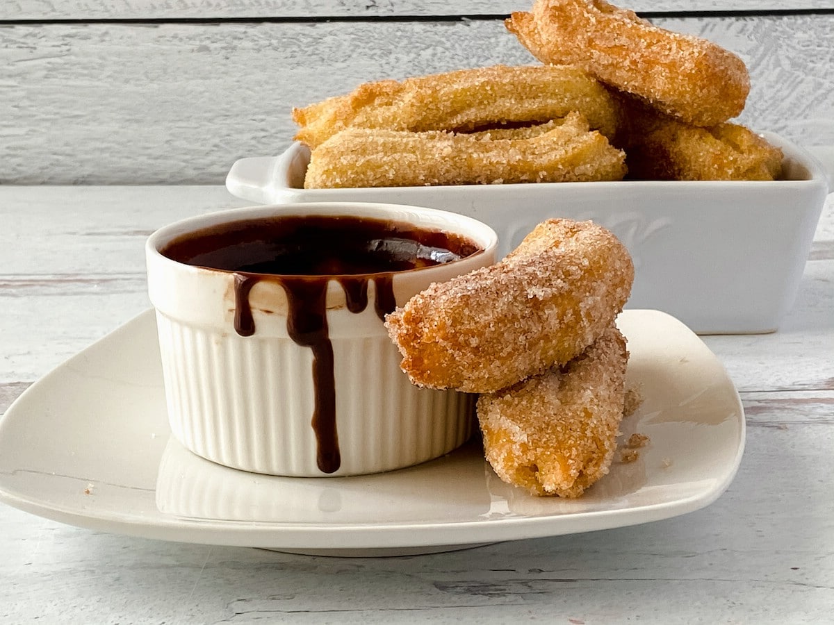 Churros on white plate by bowl of chocolate sauce
