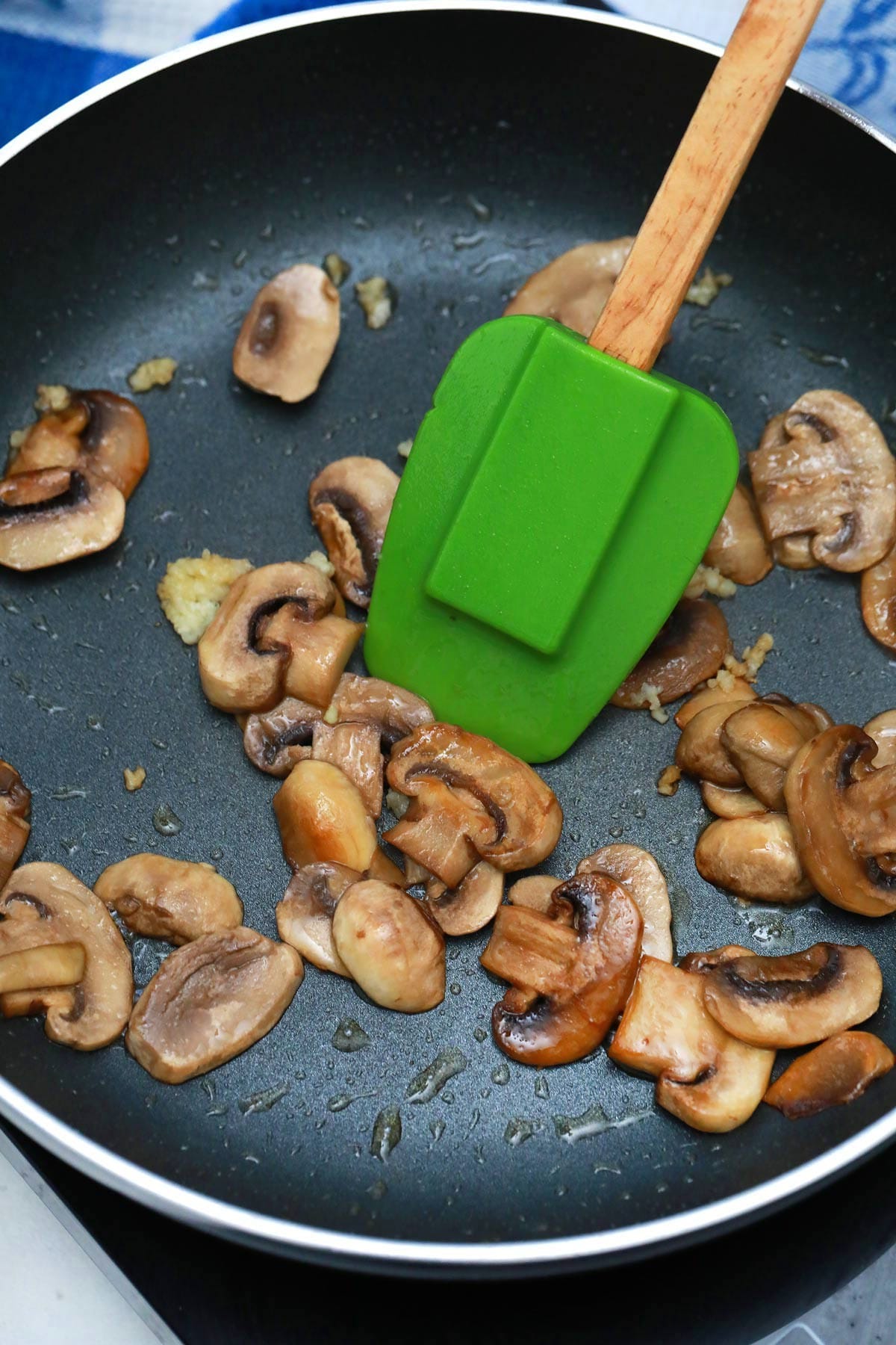 Sliced mushrooms in skillet with green spatula