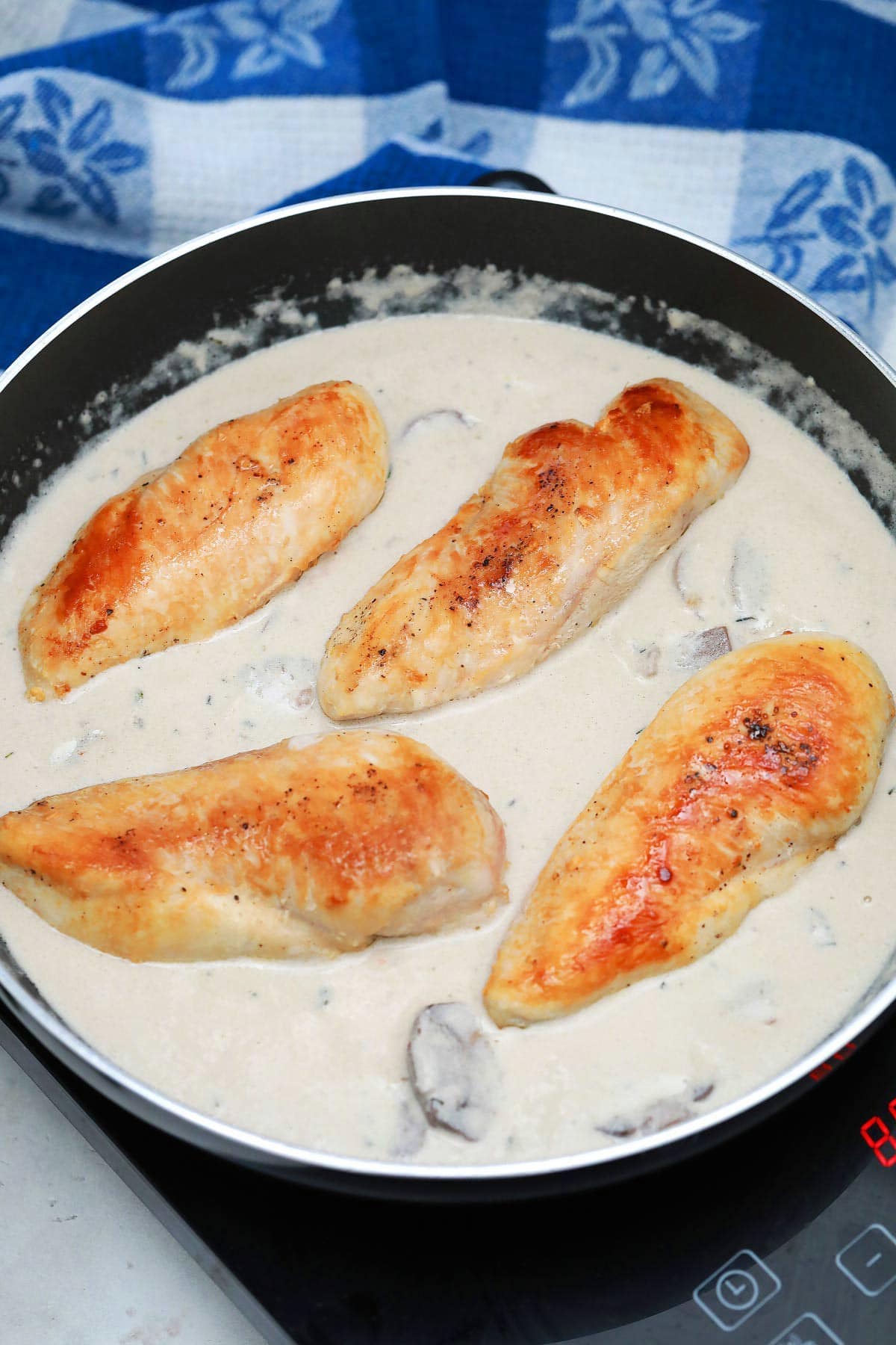 Cooked chicken breasts simmering in creamy marsala sauce