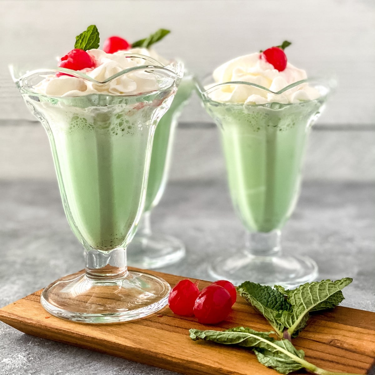 Tall clear glasses of green milkshake topped with cherry