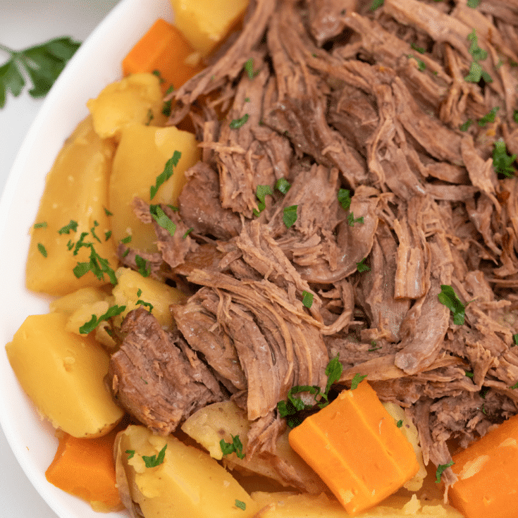 White platter filled with shredded beef roast and root vegetables