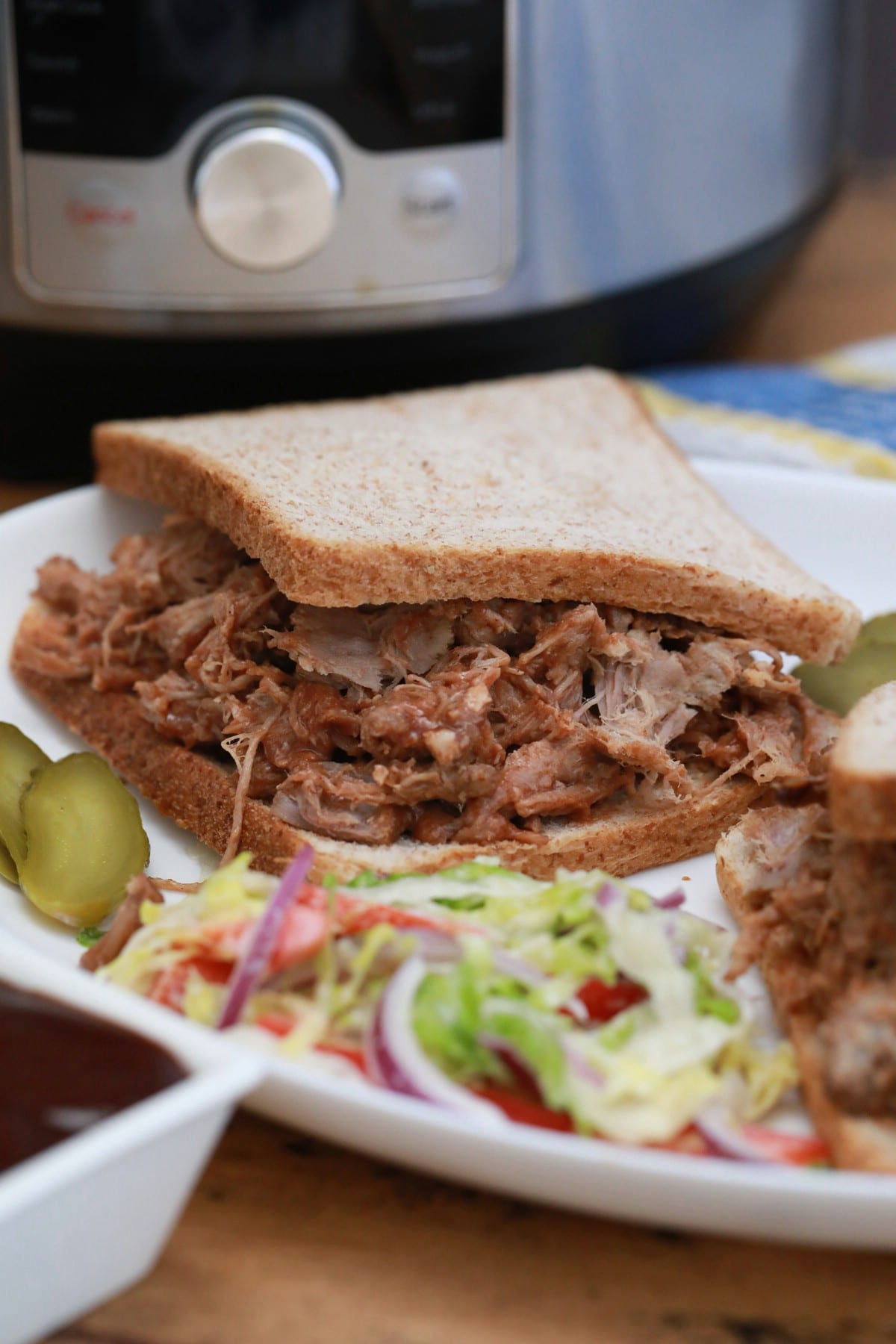 White plate with pulled pork on whole wheat and side salad