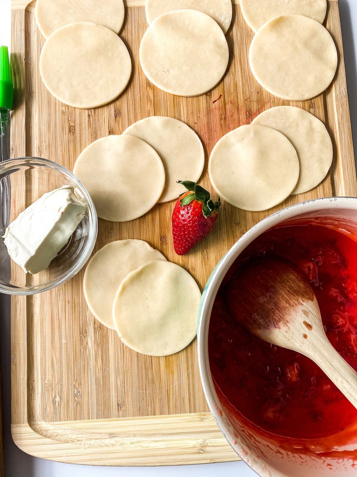 Dough rounds on cutting board by pot of strawberry jam