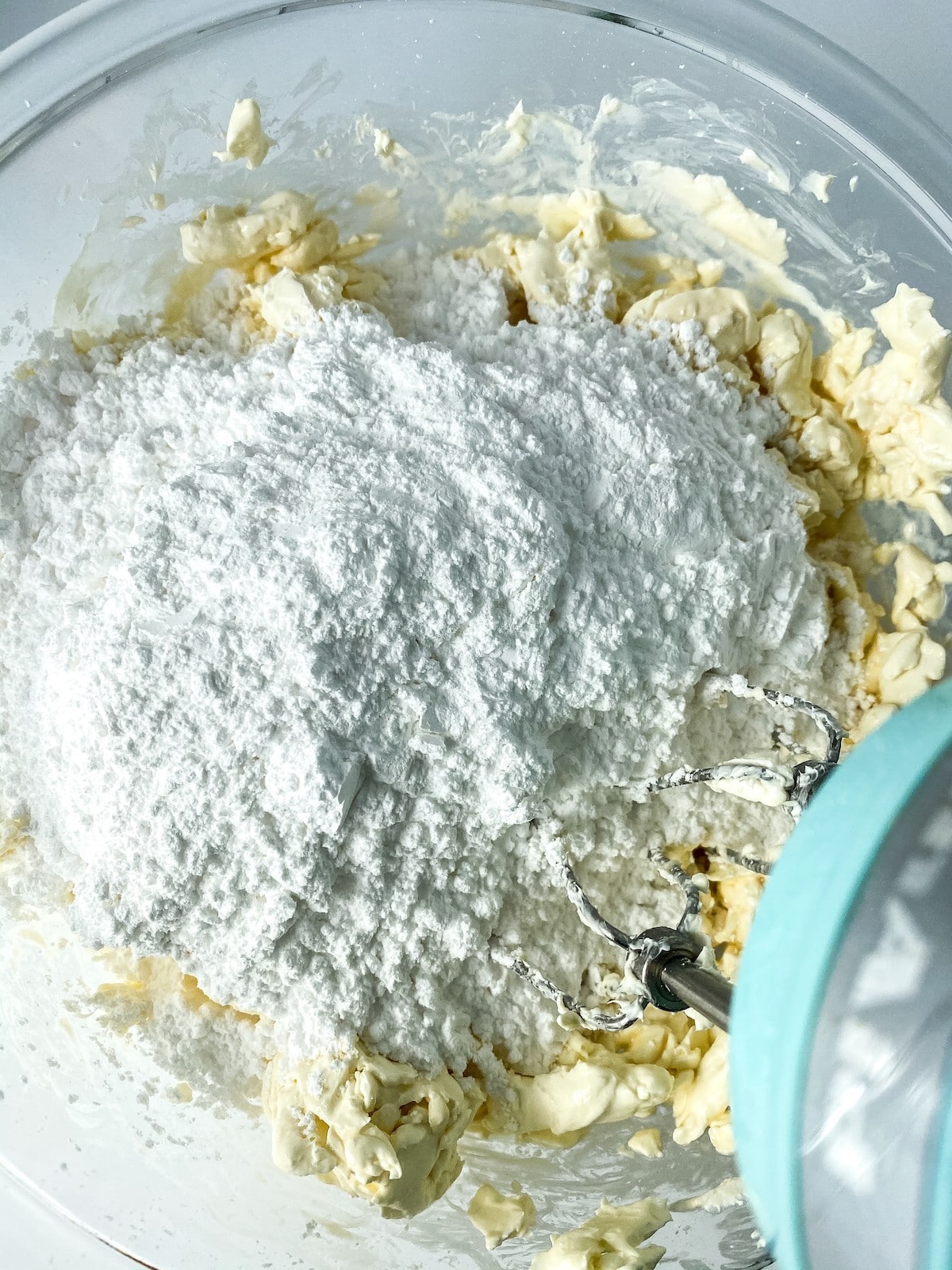 Adding powdered sugar to cream cheese in glass bowl