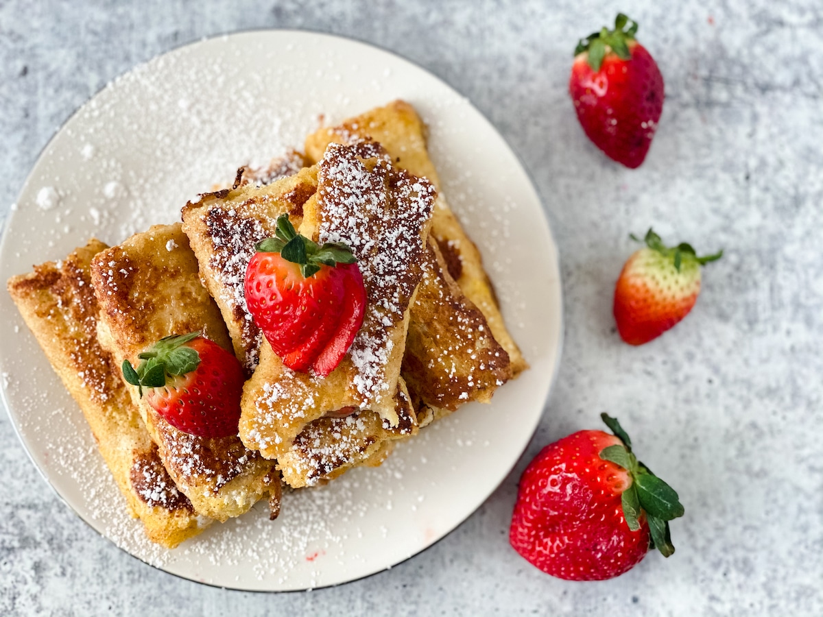 Overhead image of white plate on gray marble surface with french toast dusted in powdered sugar and berries