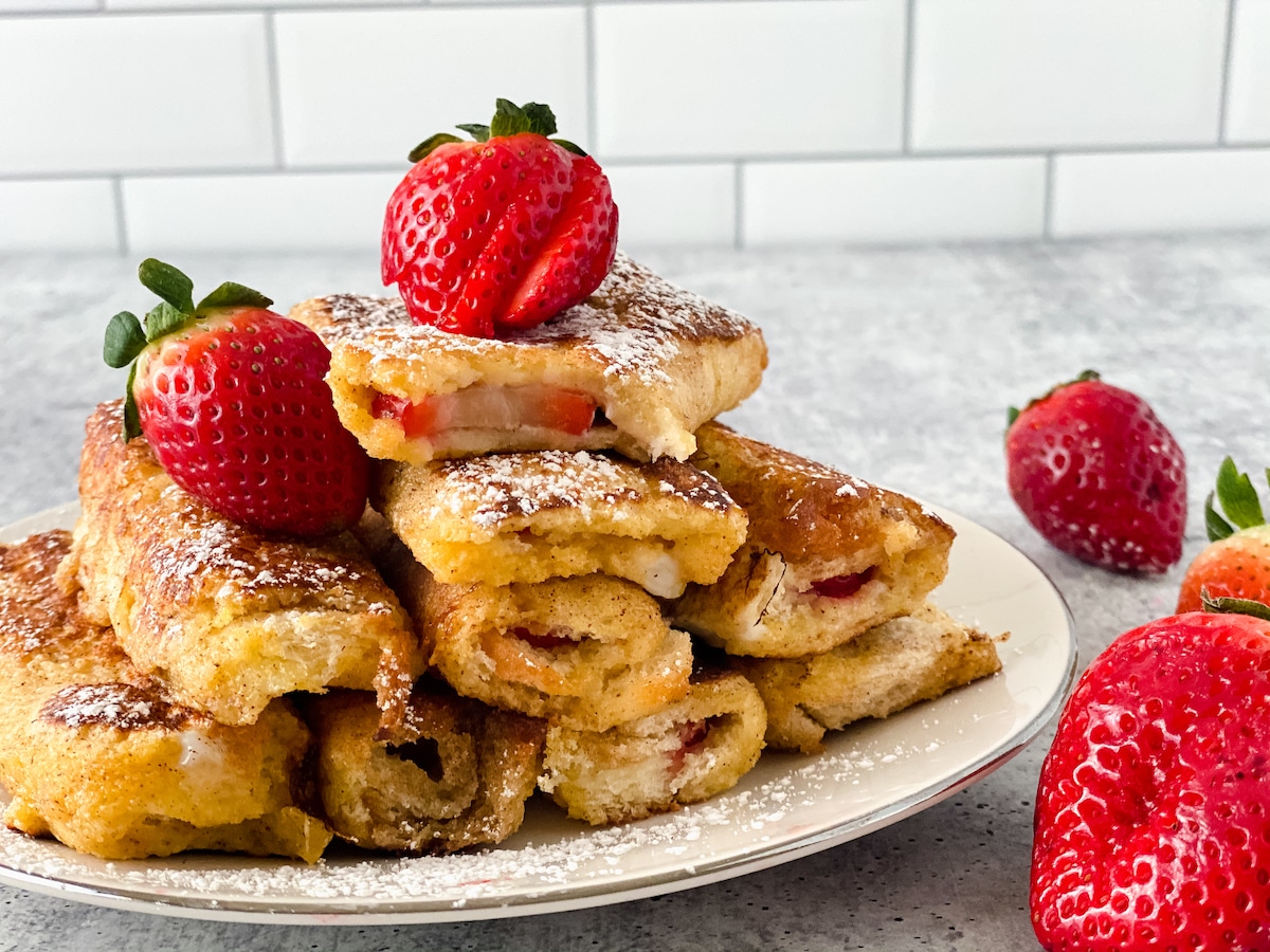 Stack of strawberry french toast on white plate dusted with powdered sugar