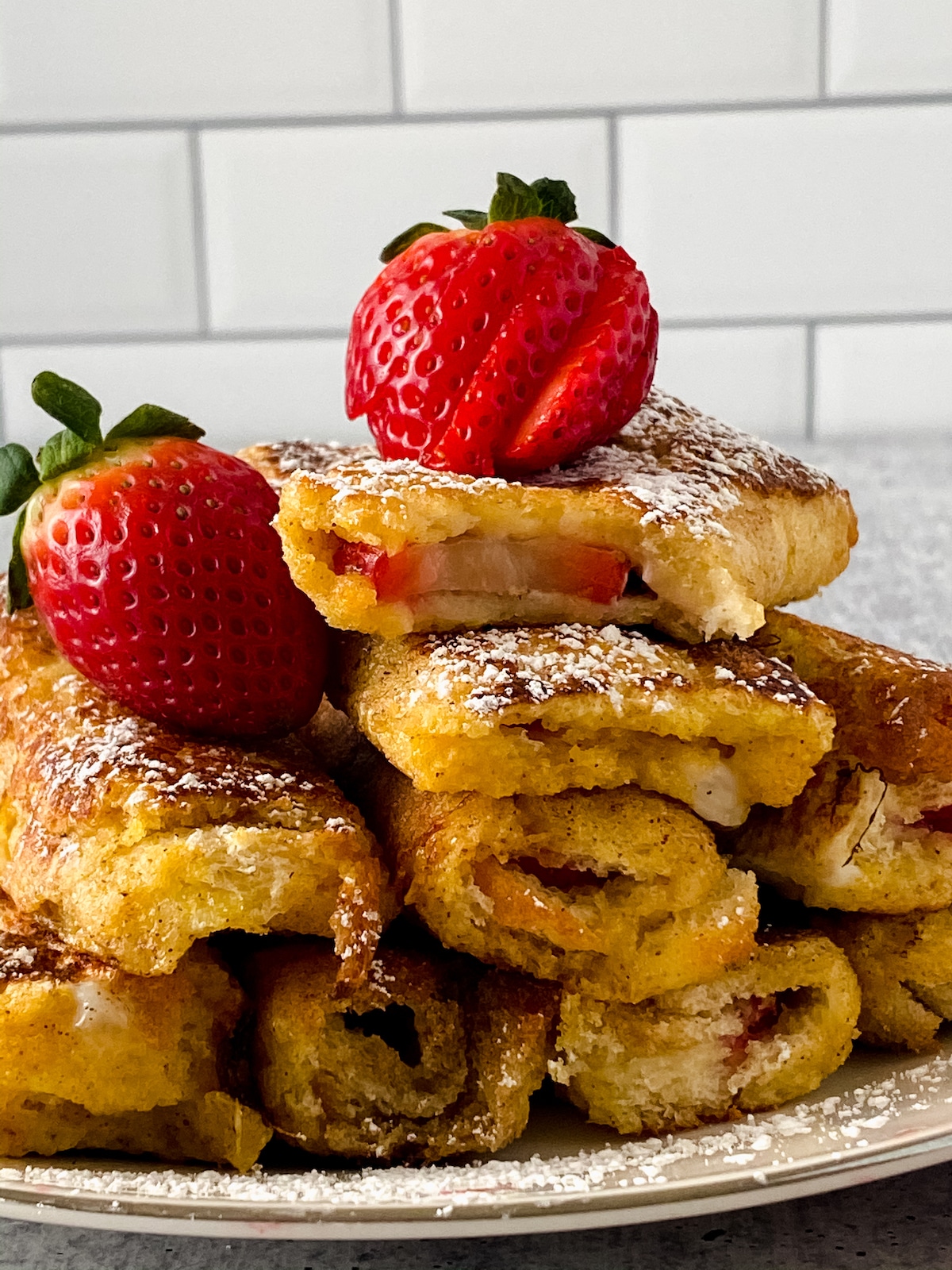French toast rolls on plate stacked with strawberry slices on top