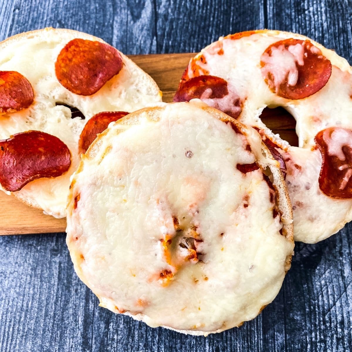 Pepperoni and cheese bagel pizzas on cutting board