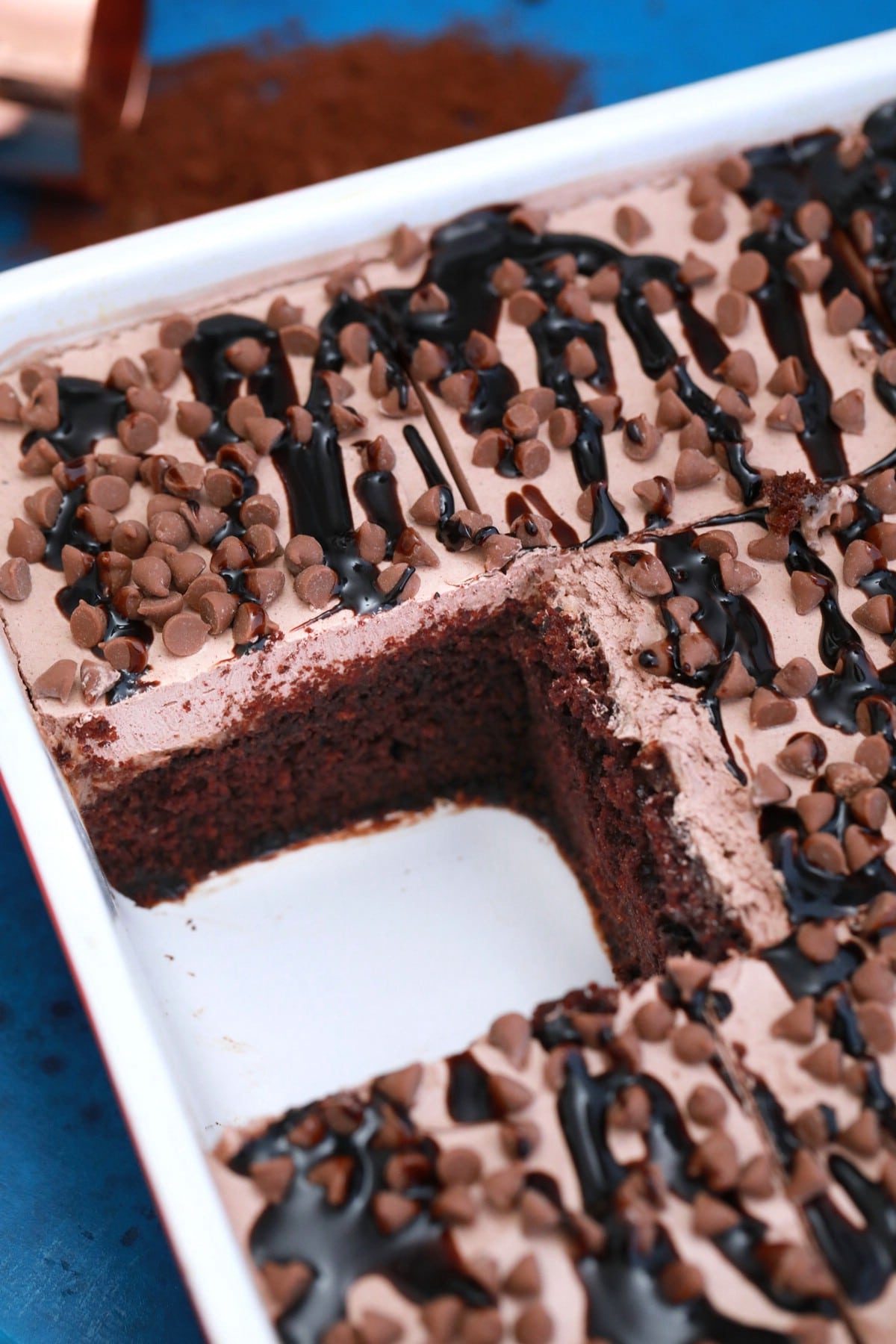 Chocolate poke cake in white baking pan with one square missing