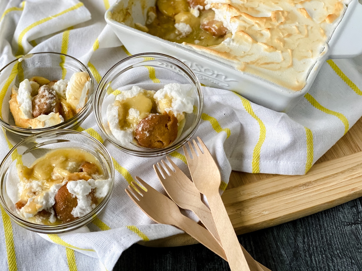 Glass bowls of baked banana pudding with wooden spoons
