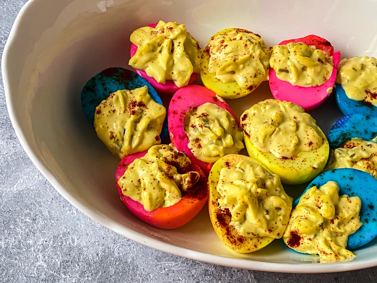 Blue and pink deviled eggs in white bowl