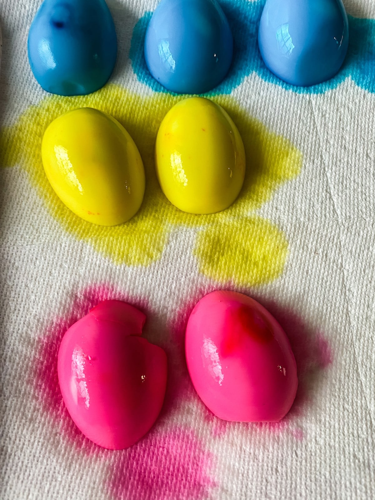 Pink yellow and blue dyed eggs draining on paper towel