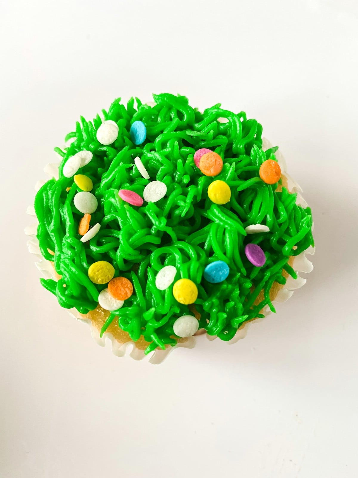 Cupcake with green icing and sprinkles on white table