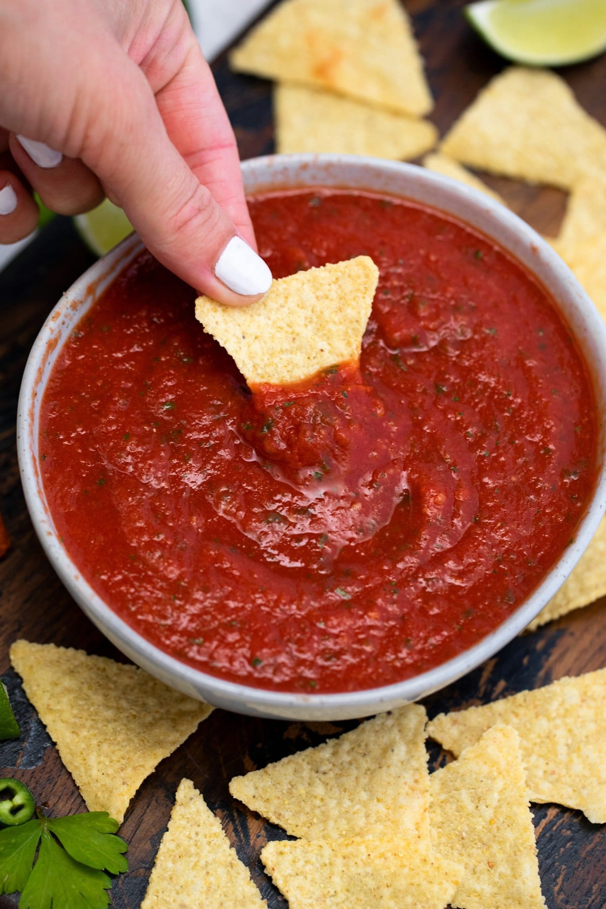 White bowl of salsa with chip dipping into salsa