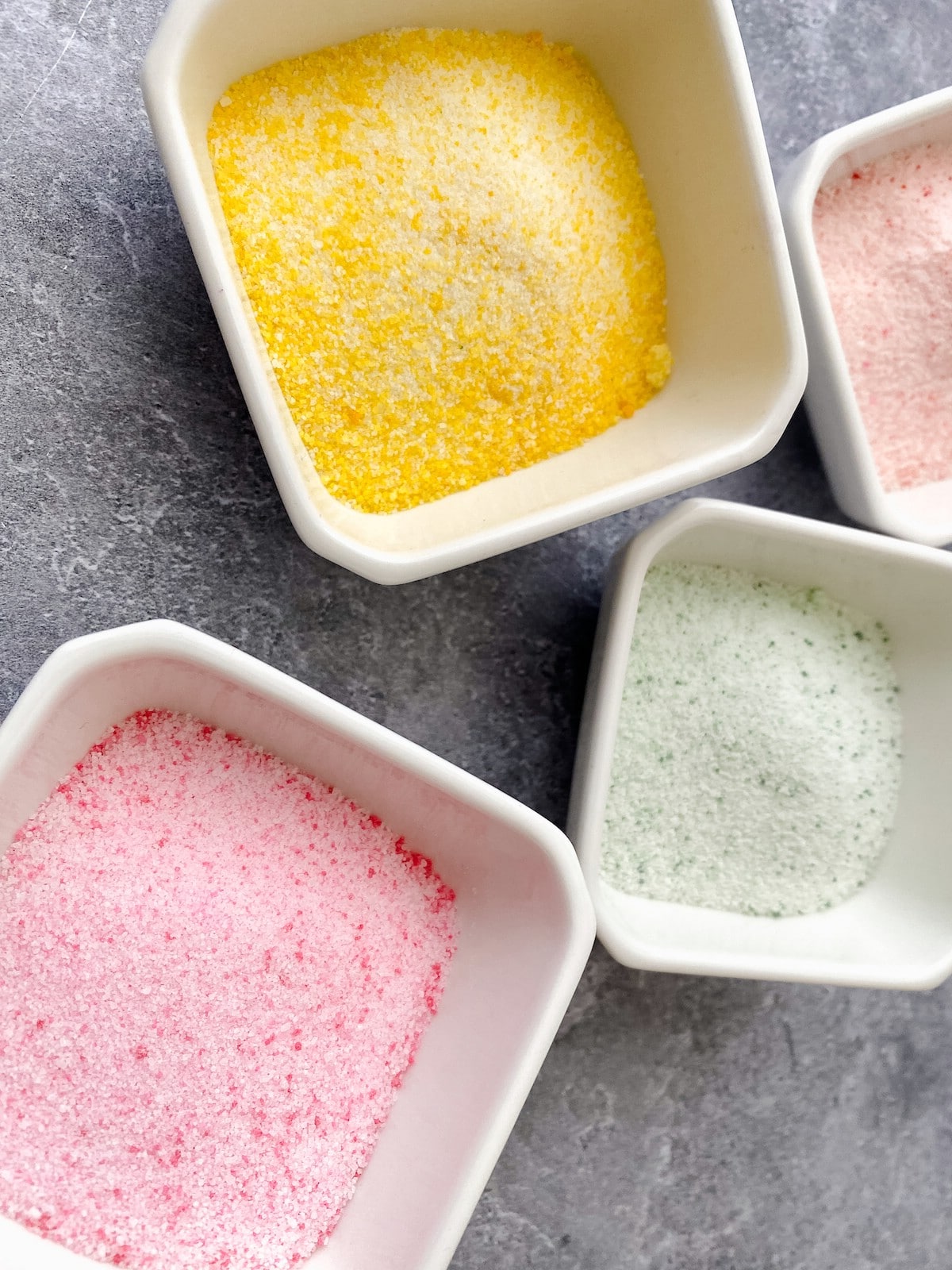 Yellow green and pink sugar in white bowls