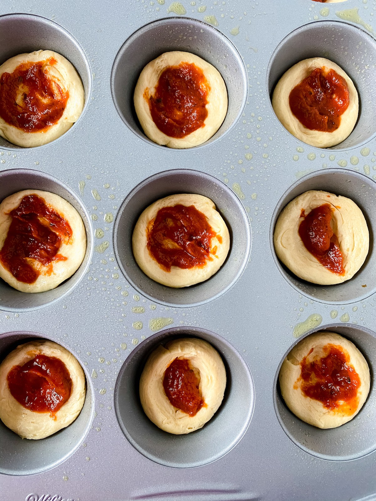 Crescent roll pieces in muffin tin topped with pizza sauce