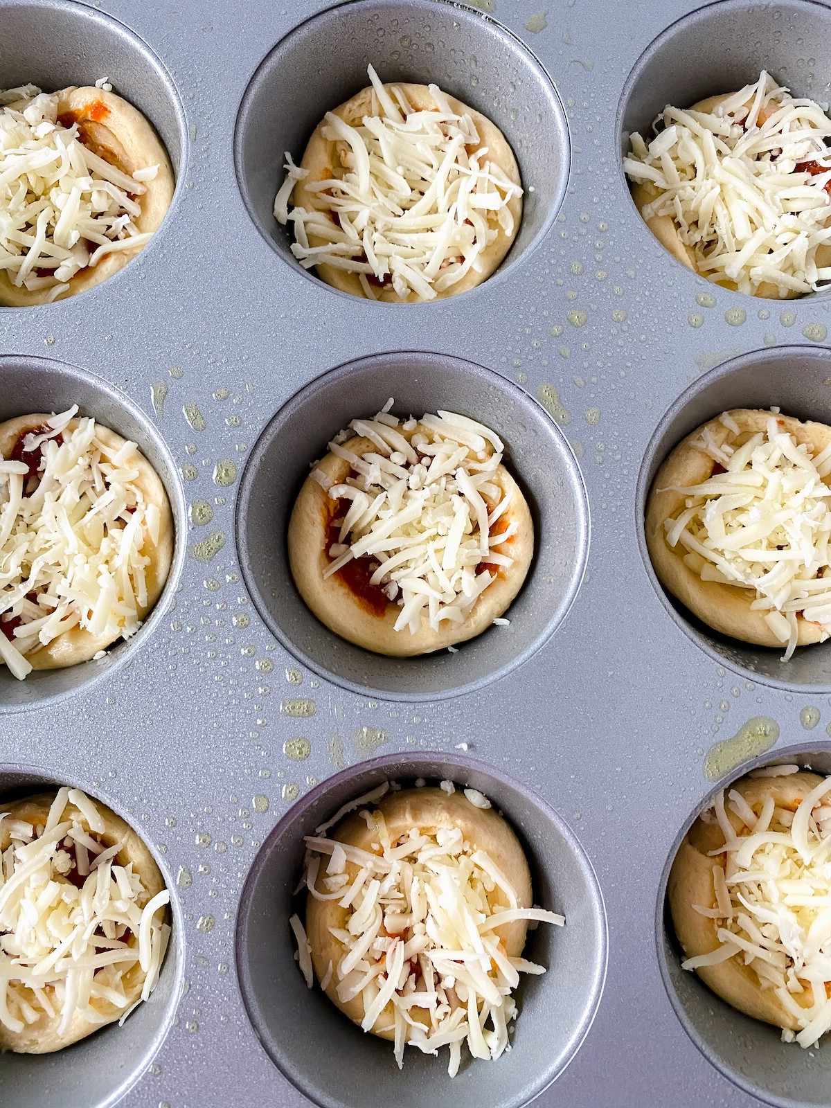 Mozzarella cheese on top of crescent roll pizza base in muffin tin