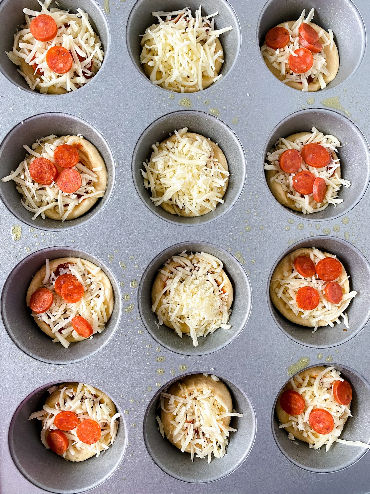 Muffin tin with crescent roll pizzas in each cavity some with pepperoni