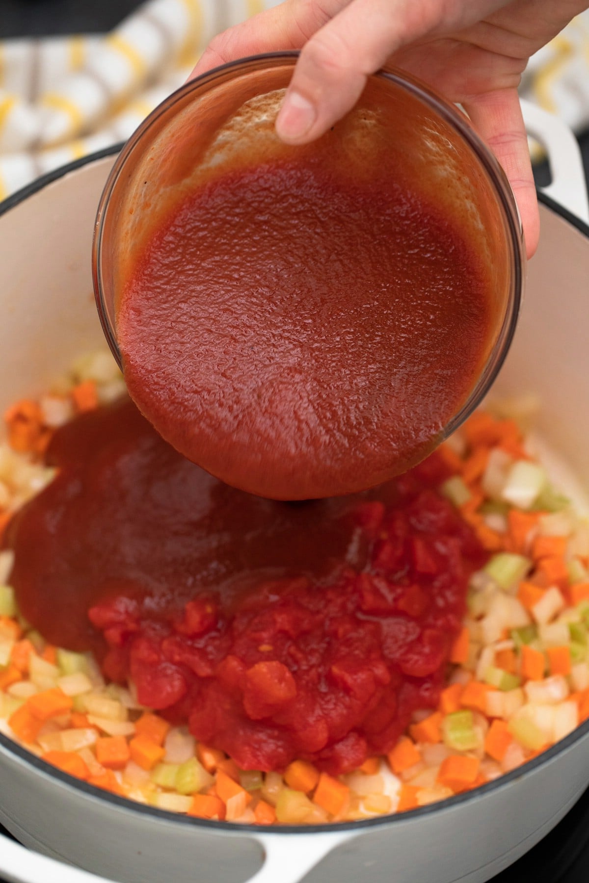 Pouring tomato sauce into pot over vegetables