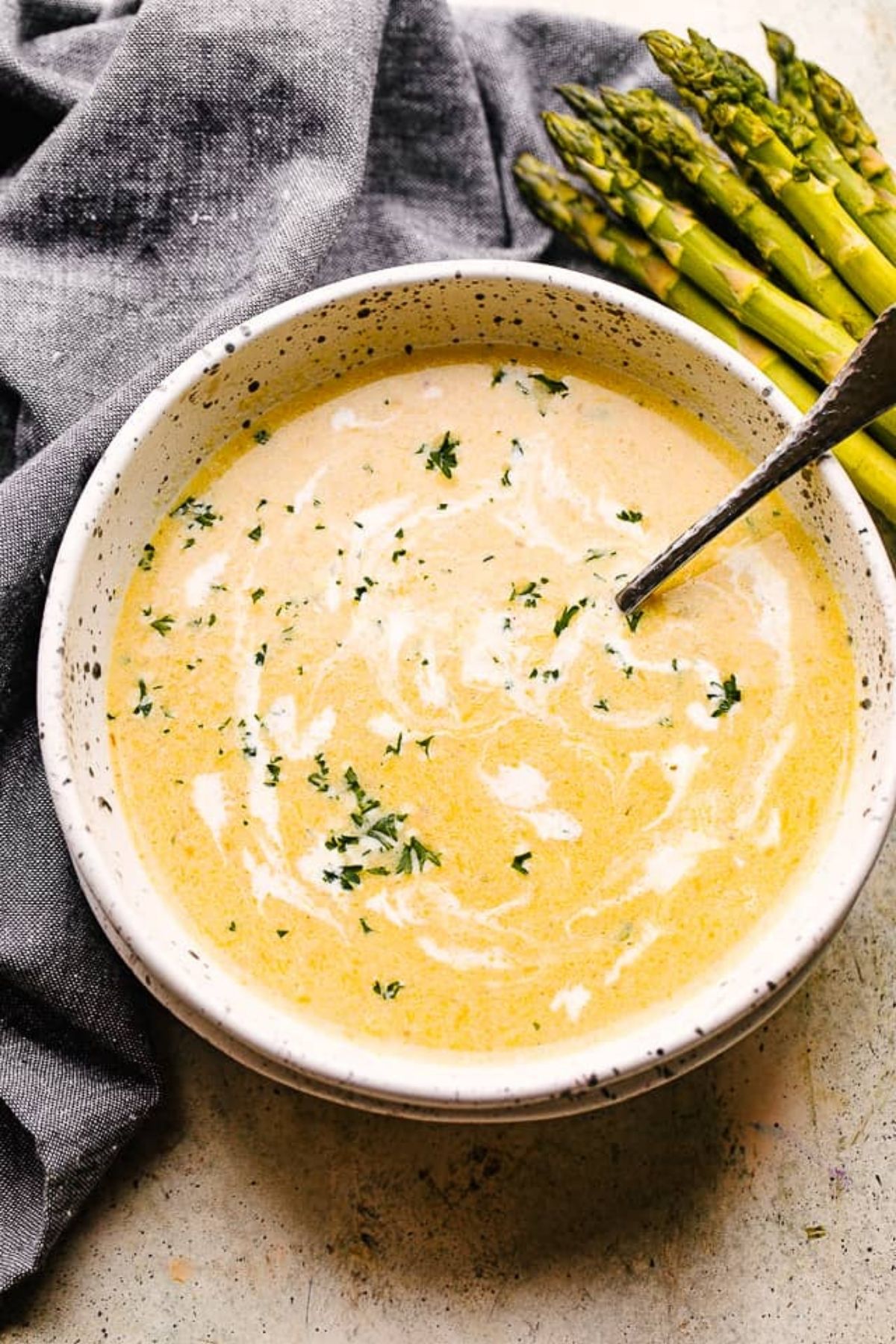 White bowl of cream soup with asparagus spears in background
