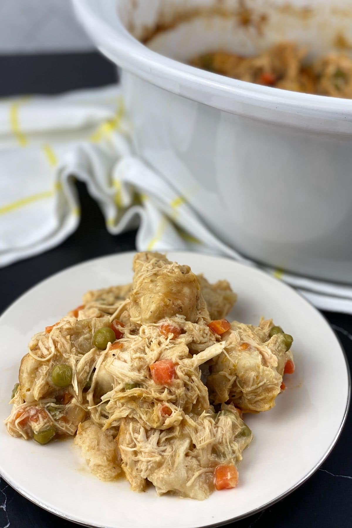 White saucer of chicken and dumplings by crock pot
