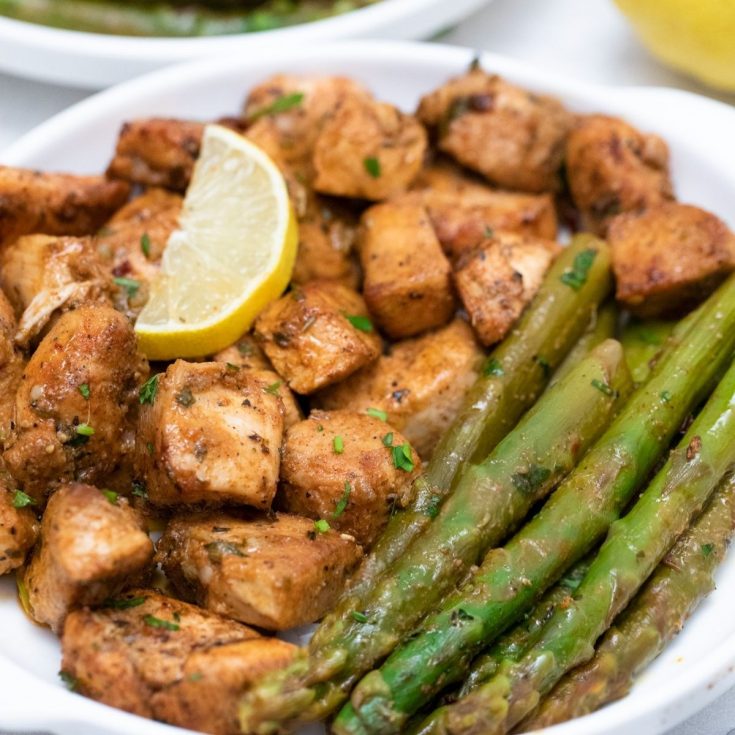 White plate with garlic butter chicken and asparagus