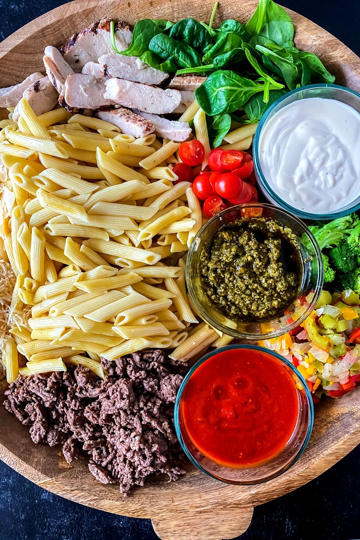 Round wooden tray with pasta and sauces in bowls
