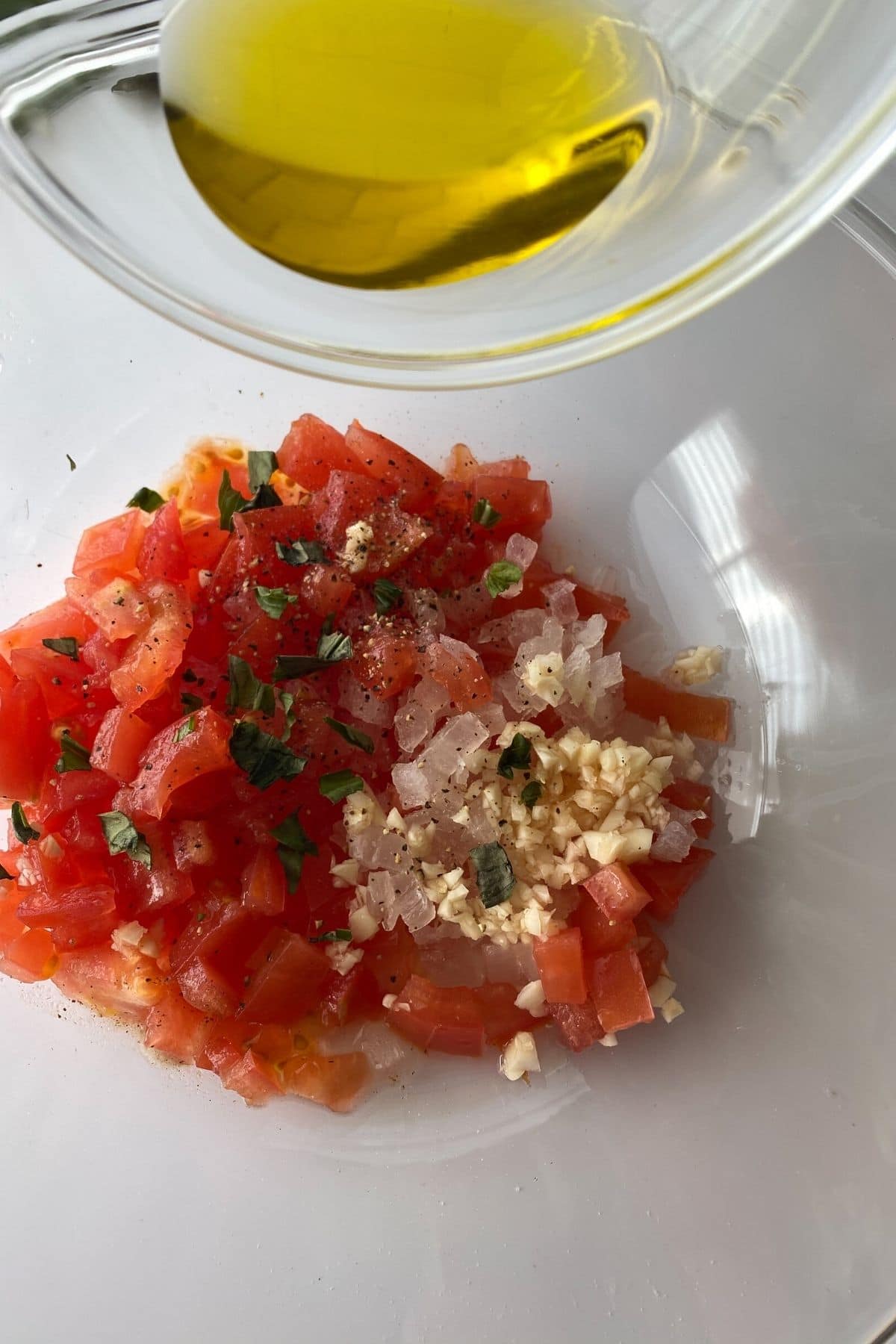 Tomato and garlic in bowl with cup of olive oil being poured over the top