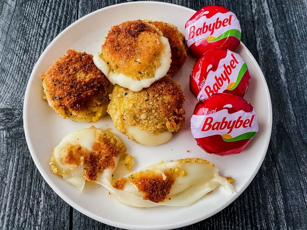 White plate on black table with babybel cheese rounds in wrapper and fried
