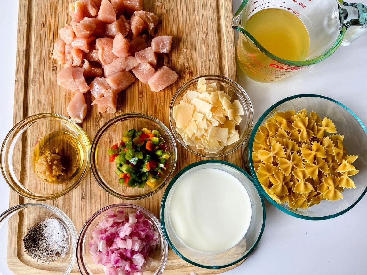 Ingredients for chicken and pasta in bowls on cutting board