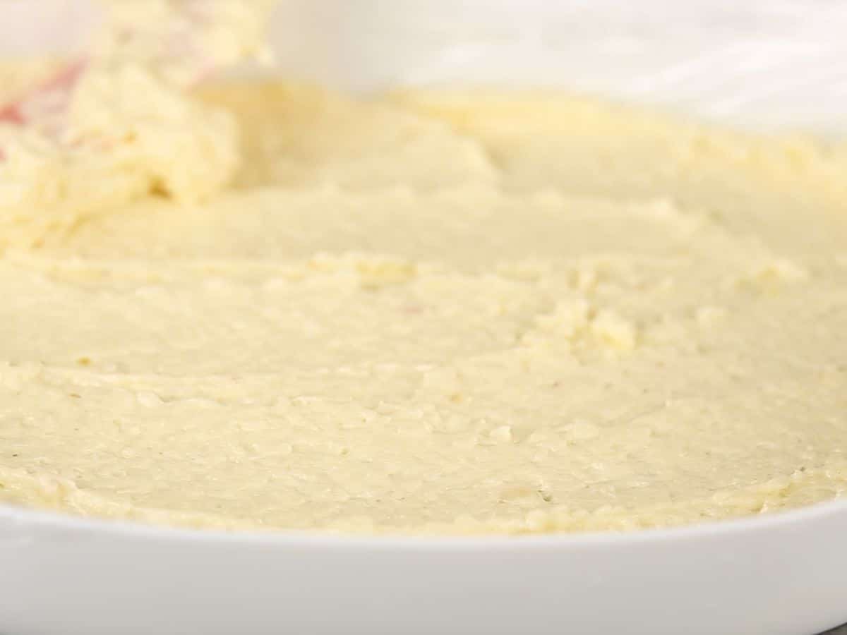 Spreading pudding mixture over biscuits in white baking dish
