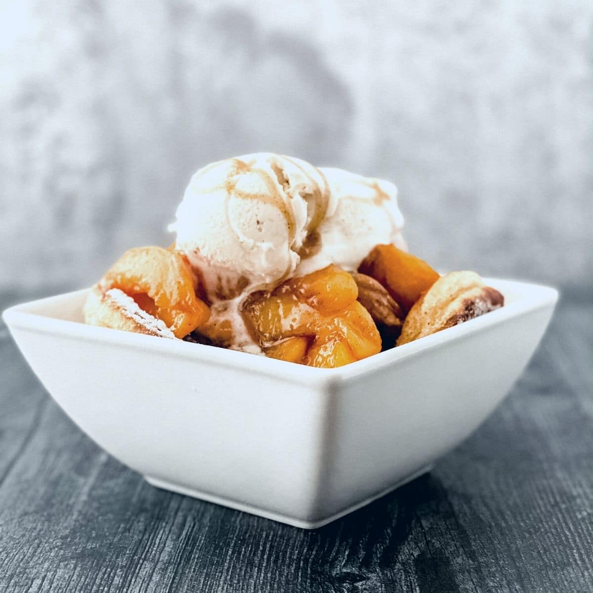 Square white bowl with peaches and ice cream on gray table
